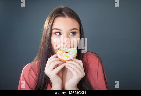 Bella ragazza adolescente tenendo premuto e tenuto un boccone fuori di una ciambella. Foto Stock