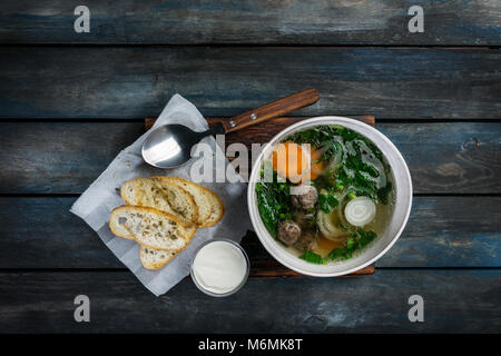 Gli spinaci e cipolla carota minestra con polpetta e pane con panna acida. Su un colore di sfondo di legno. Vista superiore Foto Stock