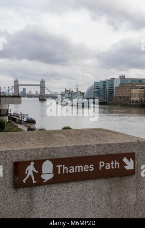 Una informazione turistica segno per il Thames Path sul lato del fiume Tamigi vicino al london bridge di londra centrale con il Tower Bridge e HMS Belfast. Foto Stock