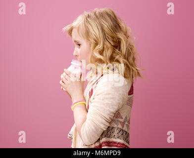 Rosa umore. Felice elegante ragazza ondulata con capelli biondi isolati su rosa azienda bere yogurt biologici Foto Stock