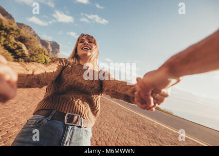 POV shot di sorridere giovane donna spinning con il suo fidanzato lungo la strada. Femmina caucasica tenendo le mani del suo ragazzo e ridere. Foto Stock