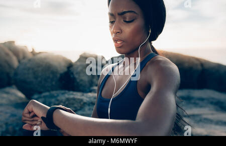 Close up della giovane donna fitness guardando il suo orologio intelligente mentre prendendo una pausa da allenamento all'aperto. Sportive impulso di controllo sulla smart fitness watc Foto Stock