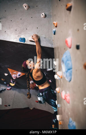 Donna bouldering in una piscina centro di arrampicata. Scalatore praticare arrampicate su roccia in una piscina palestra di arrampicata. Foto Stock