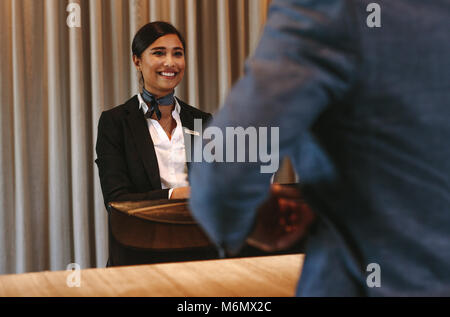 Hotel sorridente receptionist parlare con maschio ospite al banco ricevimento. Felice addetta alla ricezione lavoratore permanente al contatore di hotel con imprenditore c Foto Stock