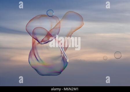 Stranamente sagomate, grandi, grandi bolle di sapone galleggianti in aria al tramonto che si affaccia sull'Oceano Pacifico, Pacific Beach, San Diego, California, USA. Foto Stock