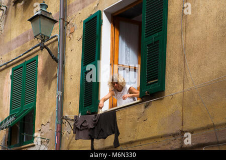 Donna pioli lavaggio fuori da un piano superiore della finestra ritagliata, Via Roma, Vernazza, Liguria, Italia Foto Stock