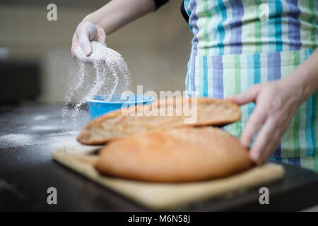 Fatto in casa pane integrale su un tavolo di legno. Donna diffondendo la farina in una ciotola. Foto Stock