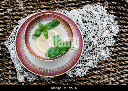 Una vista dall'alto di un teacup splendidamente realizzato con una fetta di limone e foglie di menta fresca che galleggiano nel tè, collocato su un elegante piattino Foto Stock