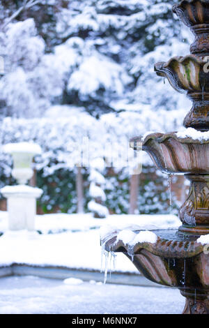 Close up, ritratto cattura di acqua congelata fontana isolato all aperto con appeso ghiaccioli, ornato giardino nevoso. Inverno magico paese delle meraviglie scena UK. Foto Stock