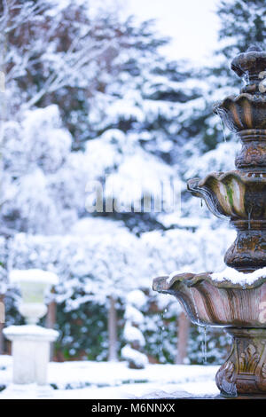 Close up, ritratto cattura di acqua congelata fontana isolato all aperto con appeso ghiaccioli, ornato giardino nevoso. Inverno magico paese delle meraviglie scena UK. Foto Stock