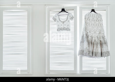 L'indiano abito da sposa, saree e camicetta appesa con le finestre bianche con luce in background. Foto Stock