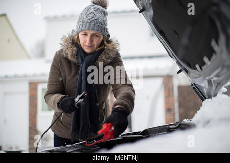 Donna che utilizza i cavi sulla batteria auto su terreni innevati giorno Foto Stock