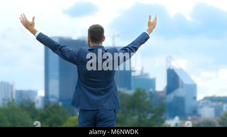 Happy business di successo uomo alza le mani, egli ha la sua vittoria di business. Sullo sfondo della grande città con grattacieli. Foto Stock