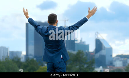 Happy business di successo uomo alza le mani, egli ha la sua vittoria di business. Sullo sfondo della grande città con grattacieli. Foto Stock