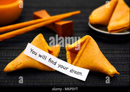 La striscia di carta con la frase che troverete il vostro sogno da Fortune cookie, un altro biscotto e bacchette sul tovagliolo nero lo sfondo. Foto Stock