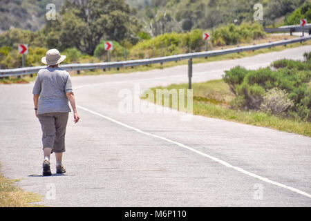 Una donna in escursionismo vestito e un cappello a piedi su un lastricato in Goukamma vicino a Knysna sulla Garden Route del Sud Africa Foto Stock