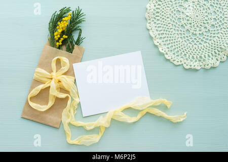 La mimosa brunch nella busta Kraft borsa su uno sfondo blu, l'arco di seta gialla con il bianco la scheda vuota per testo, uncinetto centrino Foto Stock