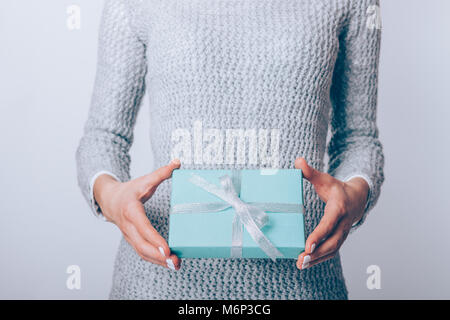 Ragazza in un maglione grigio contiene una confezione regalo in blu la carta di avvolgimento, close-up Foto Stock