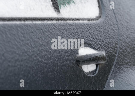 Grigio scuro porta auto coperto di ghiaccio nero in un freddo inverno mattina causato dalla pioggia gelata. Copia di potenziale spazio a sinistra della maniglia della porta. Foto Stock