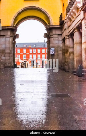 Vista di uno dei cancelli di Plaza Mayor Madrid con persone che trasportano un ombrello durante un giorno di pioggia. Foto Stock