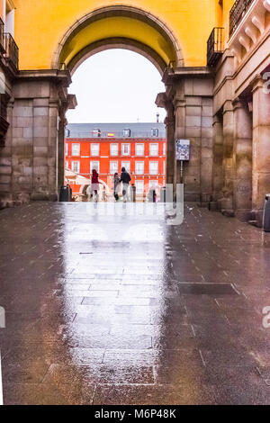 Vista di uno dei cancelli di Plaza Mayor Madrid con persone che trasportano un ombrello durante un giorno di pioggia. Foto Stock