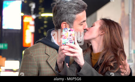 Giovane coppia attraente su data notte in Times Square a New York City, Manhattan - prendendo foto selfie baciare con smart telefono cellulare per condividere sui social Foto Stock