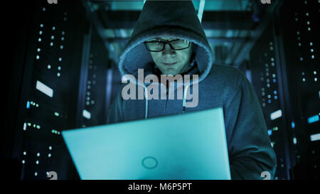 Basso angolo di close-up shot di hacker in felpa con cappuccio, tenendo il laptop. Egli Breaked in un centro dati aziendale. Foto Stock