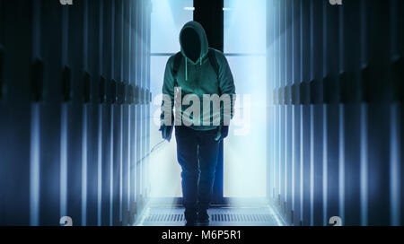 Il pirata informatico con una faccia nascosta indossando Hoodie passeggiate attraverso il centro dati di corridoio. Foto Stock