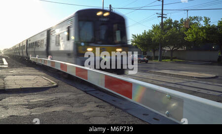Long Island, NY - Circa 2017: Ferrovia di Long Island treno attraversando porta di sicurezza xing alla stazione locale. La sfocatura in movimento ad alta velocità di transito pubblico pendolari. Mo Foto Stock