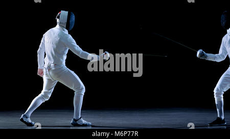 Due professionale schermitori mostrano Swordsmanship magistrale nella loro lotta di lamina. Essi Dodge, Leap e spinta affondo e. Shot isolato su sfondo nero. Foto Stock