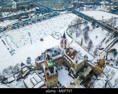 Budapest, Ungheria - Antenna vista sullo skyline di snowy Castello Vajdahunyad con City Park pista di pattinaggio su ghiaccio e Piazza degli Eroi a sfondo su un inverno mattina Foto Stock