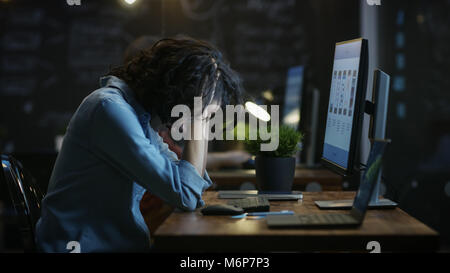 Stanchi, affaticati femmina Telefono Mobile App Designer mantiene la sua testa nelle mani mentre si lavora su un Personal Computer. In Background Creative Office. Foto Stock