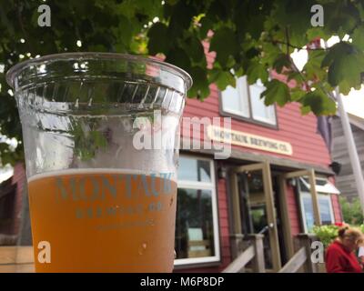 Long Island, NY - Circa 2017: Montauk Brewing Company edificio in background di coppa del marchio per la birra campione in corrispondenza al di fuori del giardino della birra a campione e gusto n Foto Stock