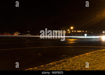 Esposizione lunga scia luminosa di notte il traffico su una tranquilla cittadina main street durante una pioggia di nebbia Foto Stock