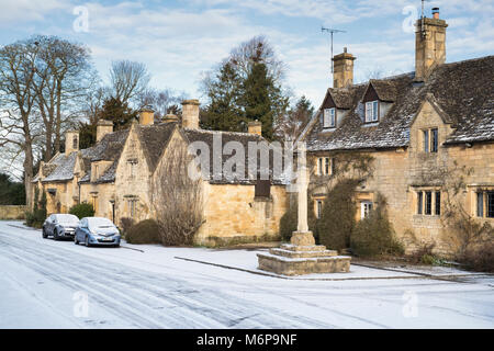 Stanton case in pietra e croce medievale nella neve d'inverno. Stanton, Cotswolds, Worcestershire, Inghilterra Foto Stock