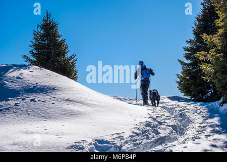 Escursionista maschio con giacca blu e backbag passeggiate con il cane nero attraverso la neve profonda sulla montagna Rennfeld in inverno Foto Stock