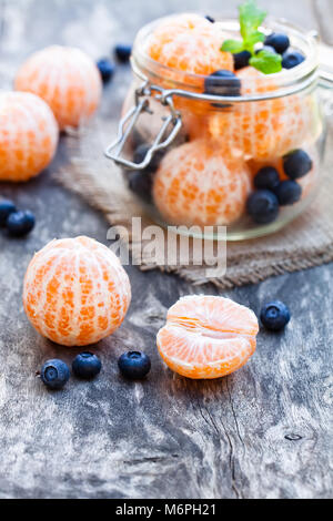 Sbucciate mandarino o mandarino e frutta mirtillo nel vasetto di vetro sul tavolo di legno Foto Stock