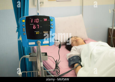 Focus sul monitor della pressione del sangue con paziente femmina sul letto in ospedale. Concetto medico Foto Stock