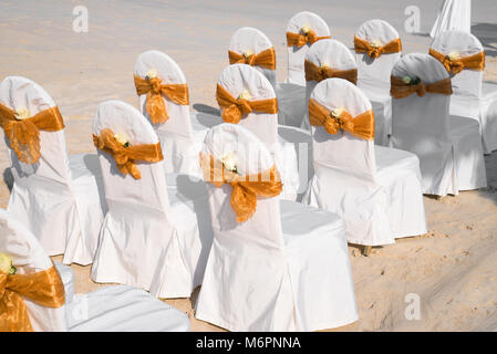Un gruppo di bianco spandex sedie coprire con oro organza anta spiaggia per matrimoni, il cono di petali di rose Foto Stock