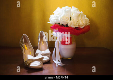 Il bouquet della sposa con crema di rose e la sposa scarpe, sul pavimento in legno con sfondo giallo, la luce dalla parte superiore Foto Stock