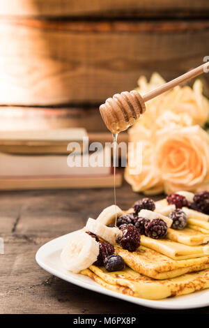 Frittelle di banane e frutti di bosco surgelati su sfondo scuro. crepes con le banane e la frutta Foto Stock