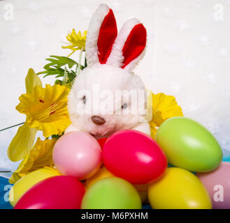 White coniglio peluche con colorate le uova di Pasqua e fiori di colore giallo. Foto Stock