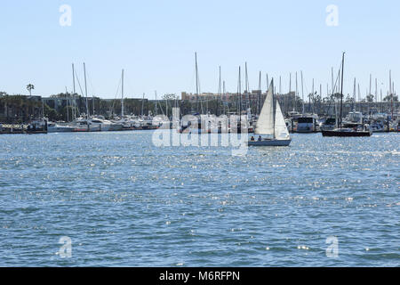 Una barca a vela attraverso Marina Del Rey California in un pomeriggio soleggiato con molte barche e yacht ormeggiati in background Foto Stock
