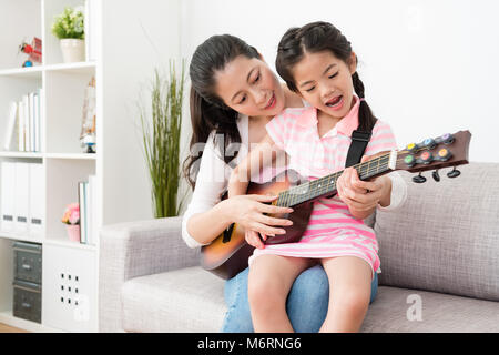 Madre figlia insegna come suonare la chitarra e poco ragazza asiatica trattare anche la parte vocale delle prestazioni. Essi praticano il loro talento sho Foto Stock