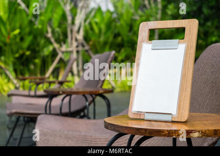 Cornice menu vuota in piedi su un tavolo di legno nella caffetteria all'aperto vicino al giardino, spazio di copia per il testo Foto Stock