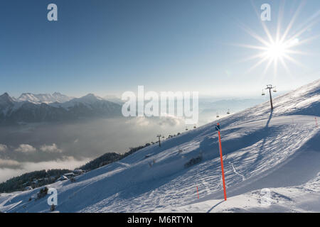 Bella giornata in profonda inverno in una località sciistica nelle Alpi con un impianto di risalita e le piste da sci e il sole che splende Foto Stock