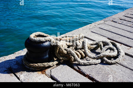 Dock con il vecchio annodato legata la cima di ormeggio vicino al mare blu Foto Stock