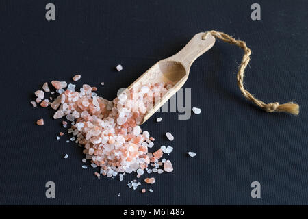 Himalayan rock salt e scoop di legno vicino sul nero sfondo rustico Foto Stock