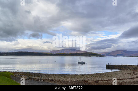 La vista da Nord di Port Appin guardando verso l'isola di Lismore e le montagne al di là. Uno yacht si trova ormeggiata in acque calme di Loch Linnhe. Foto Stock