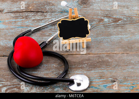 Uno stetoscopio con cuore rosso e lavagna con spazio vuoto per un testo sullo sfondo di legno. Foto Stock